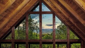 Un dormitorio de ático con ventanas amplias que ofrecen vistas a un paisaje boscoso.