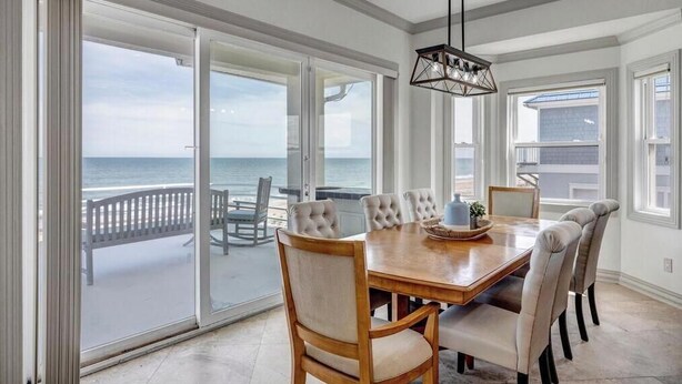 A dining area with a large table and chairs, a hanging light fixture, and a view of the ocean through large sliding doors. - Sea Haven - Oceanfront home w/beach access & deck (Ponte Vedra Beach)