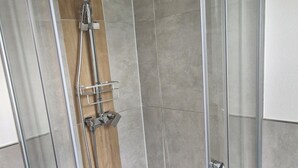 Eine Eckdusche mit Glastrennwand, einer Handbrause und einem am Wand montierten Wasserhahn.