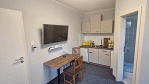 Eine kleine Küche mit Holztisch und -stühlen, einem integrierten Fernseher und weißen Schränken.