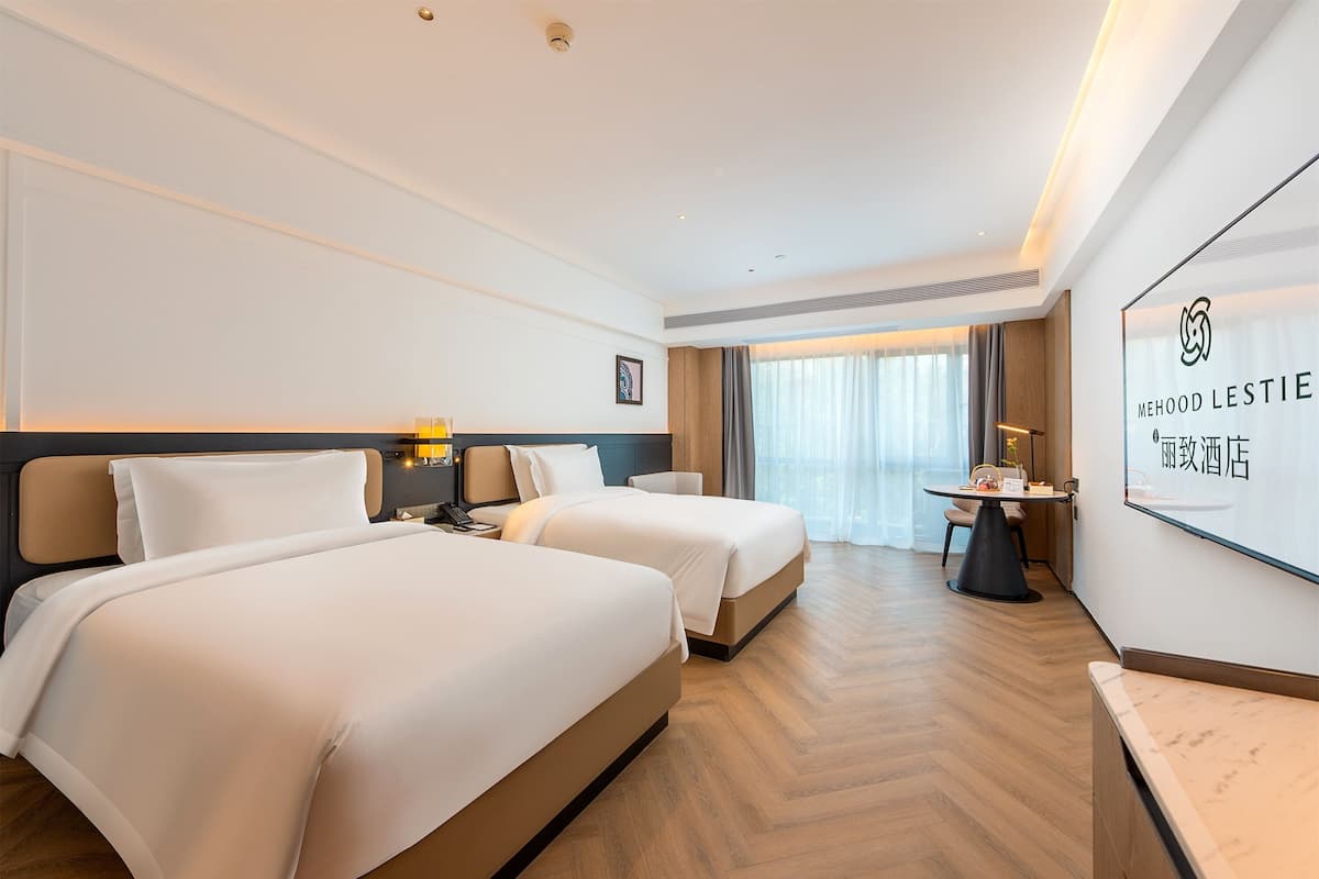 Una camera d'albergo con due letti, una scrivania e un'ampia finestra con tende.