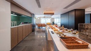 A modern hotel kitchen with a long counter, various food items, and a seating area in the background. - MEHOOD LESTIE Hotel Guangzhou Tianhe Financial City (Guangzhou)