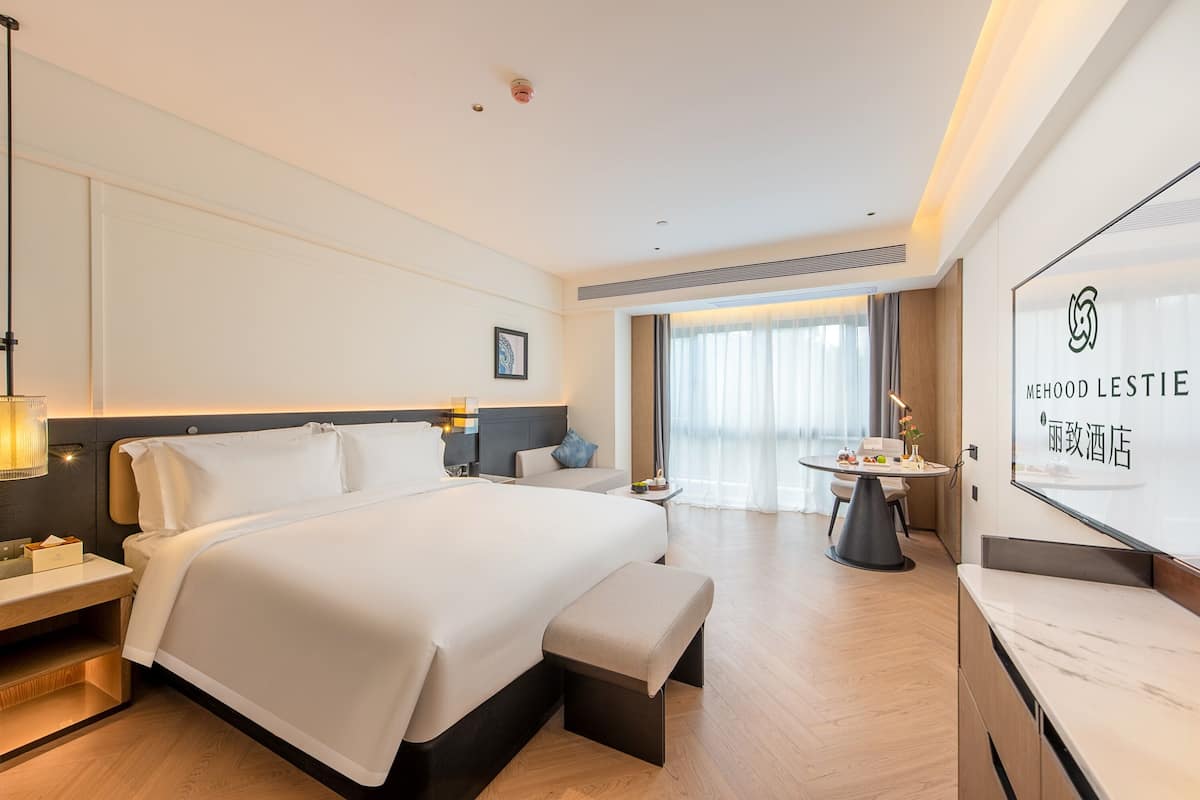 Camera d'hotel moderna con un ampio letto, comodini, una piccola scrivania e vista sulla città attraverso ampie finestre.