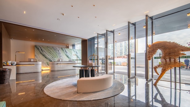 A modern hotel lobby with a reception desk, a round seating area, and a large glass window offering a view of the city. - MEHOOD LESTIE Hotel Guangzhou Tianhe Financial City (Guangzhou)