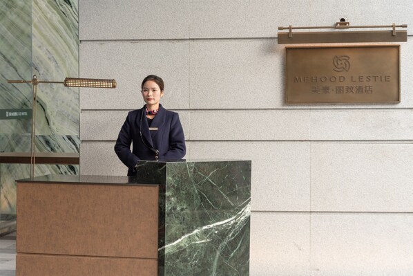 A person standing at a podium with a sign above reading "MEHOOD LESTIE".