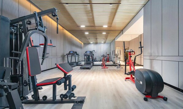 Un gimnasio moderno con diversos equipos de ejercicio, incluyendo cintas de correr, máquinas de pesas y una banca.