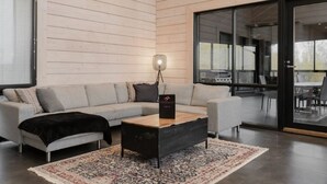 A modern living room with a light-colored wooden wall, a grey sofa, a black coffee table, and a patterned rug. - Villa Nevada, Northwest-Himos Ski-in/out (Jämsä)