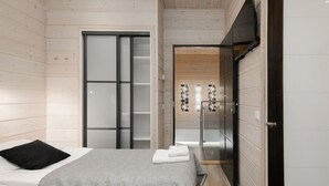 A modern bedroom with a bed, a wardrobe, and a bathroom with a glass door. - Villa Nevada, Northwest-Himos Ski-in/out (Jämsä)