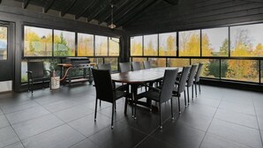 A spacious patio with a large table and chairs, a grill, and a view of autumn trees through large windows. - Villa Nevada, Northwest-Himos Ski-in/out (Jämsä)