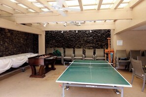 Een kamer met een tafeltennistafel, stoelen, een tafelvoetbaltafel en een stenen muur.