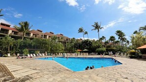 A swimming pool surrounded by palm trees and lounge chairs, with a hotel building in the background. - Kamaole Sands #4-110 Ground Floor, Full A/C, Great Location, Fitness Center! (Kihei)