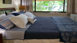 A hotel room with a bed, a ceiling fan, a window with curtains, and a view of greenery outside. - Kamaole Sands #4-110 Ground Floor, Full A/C, Great Location, Fitness Center! (Kihei)