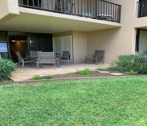 A covered outdoor patio with a seating area, a small garden, and a grassy lawn.
