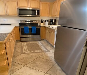 A kitchen with wooden cabinets, a stainless steel refrigerator, a microwave, and an oven.