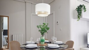 A dining area with a round glass table, six wicker chairs, a hanging light fixture, and a potted plant.