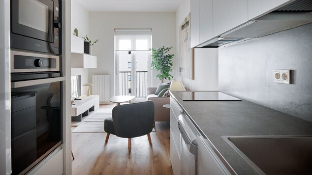 A modern kitchen with a built-in oven, a dining area with a round table and chairs, and a large window providing natural light.