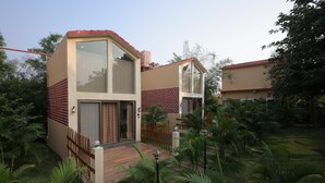 Una casa moderna de dos pisos con techo rojo, ventanas grandes y terraza de madera.