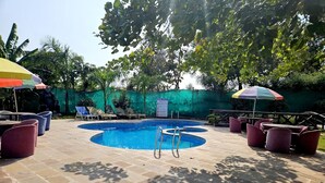 Piscina exterior con sillas de descanso y sombrillas, rodeada de vegetación y un sendero de piedra.