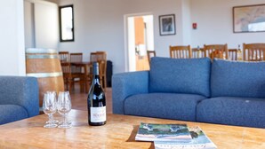 A room with a blue sofa, a wooden table with a wine bottle and glasses, and a dining area in the background. - Gîte Cévennes 2*, Pic Saint Loup (Vacquières)