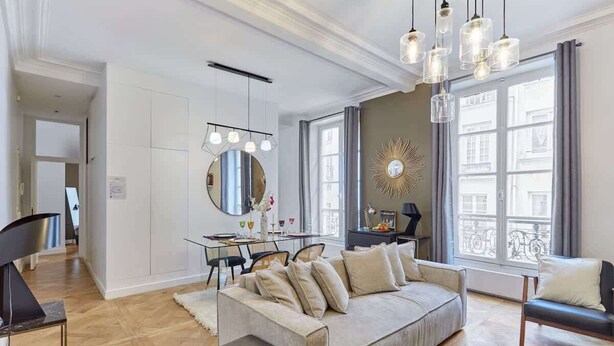 A modern living room with a sofa, a dining table, and a large window with curtains.