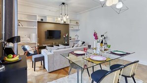 A modern living room with a sofa, a glass dining table set for four, and a TV in the background.