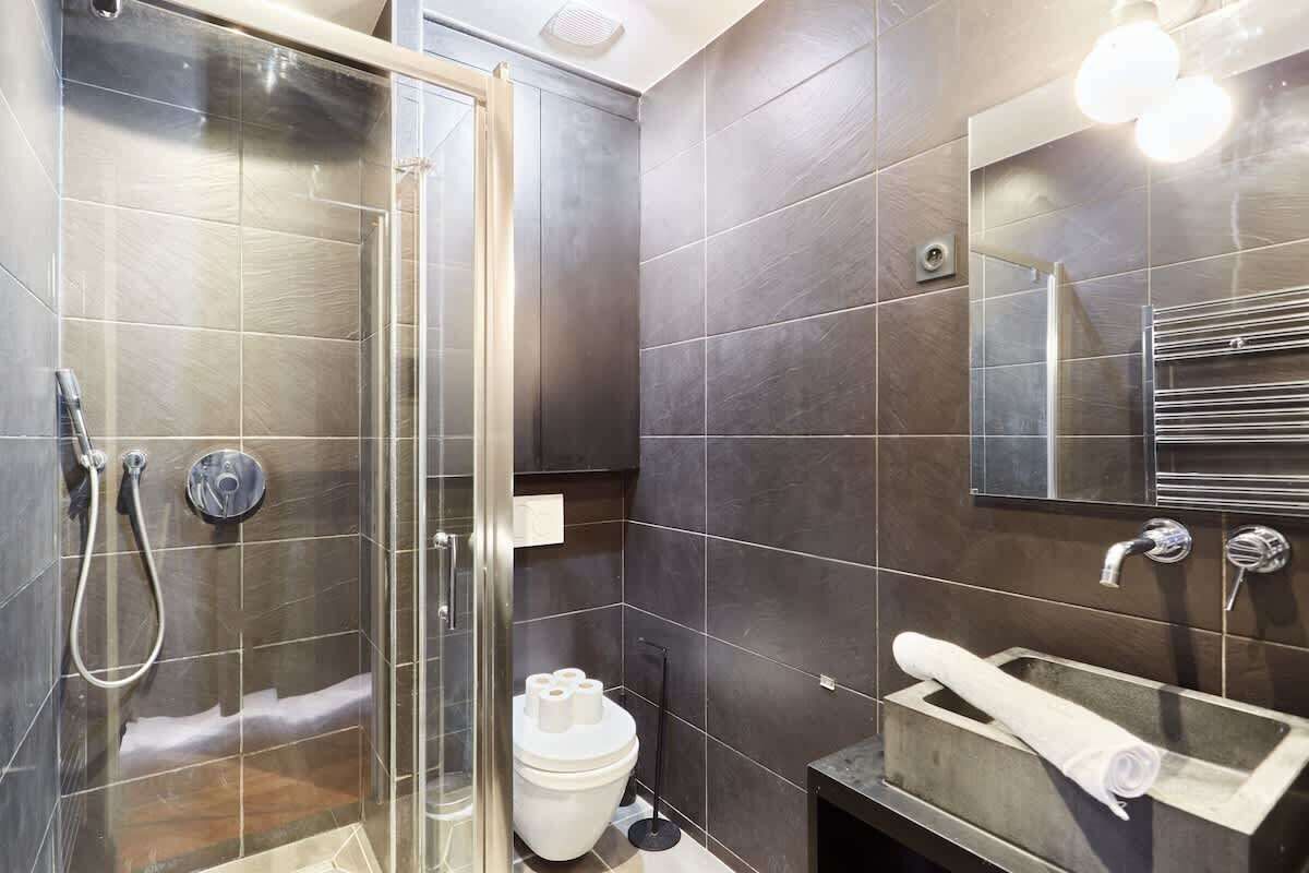 A modern bathroom with a glass shower enclosure, a toilet, a sink with a towel, and a mirror.