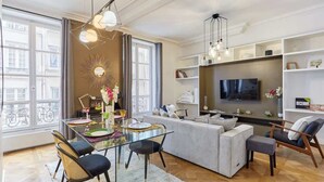 A modern living room with a glass dining table, a sofa, and a TV mounted on the wall.