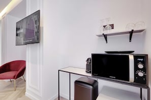 A modern room with a flat-screen TV mounted on the wall, a microwave on a small table, a red chair, and a shelf with wine glasses.