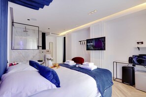 A modern hotel room with a large bed, a TV, a small desk with a computer, and a minibar. - Suberb Suite with Jacuzzi Le Marais Beaubourg (Paris)