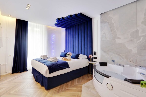 A modern hotel room with a large bed, a bathroom with a bathtub, and a marble wall.
