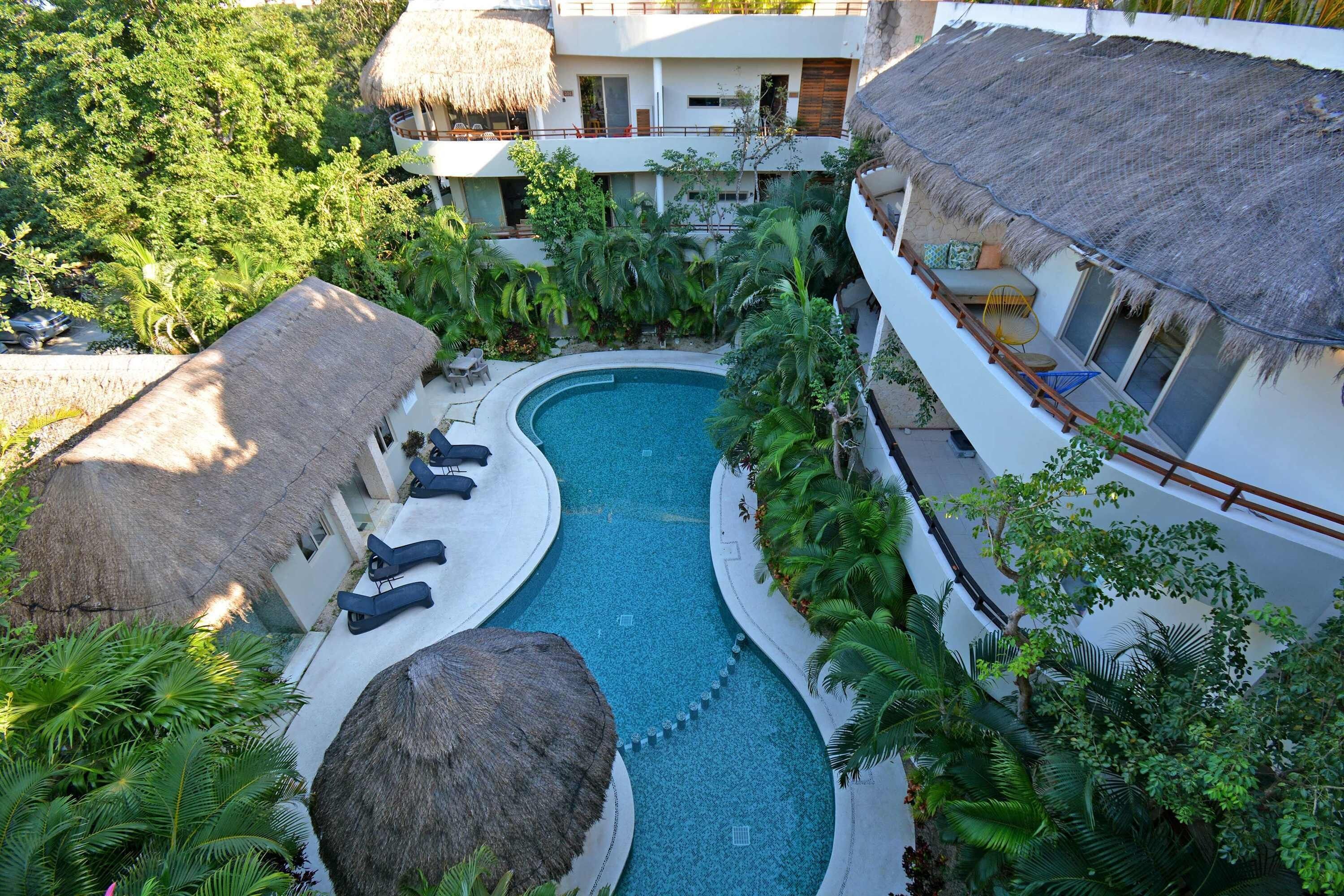 A resort with a central swimming pool, lounge chairs, and thatched-roof structures.
