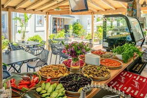 Un bufé con diversas opciones de comida, una máquina de café y mesas al aire libre.