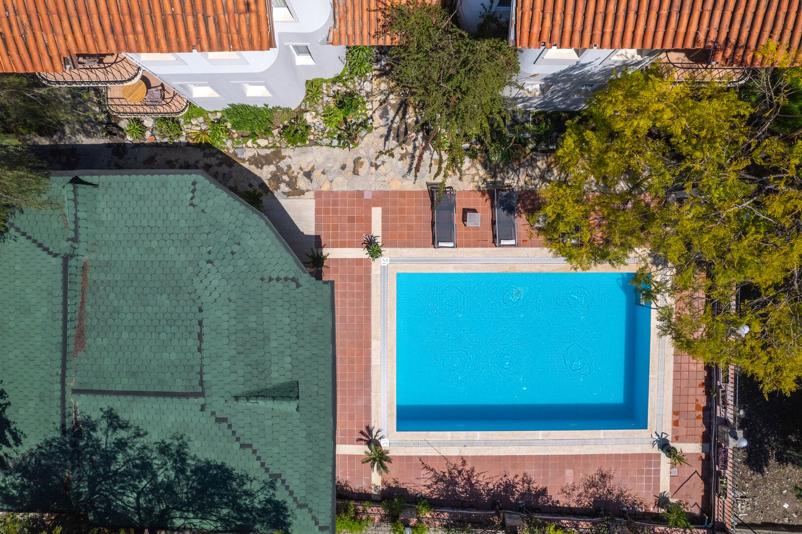 An aerial view of a property with a swimming pool, a tennis court, and a garden area.