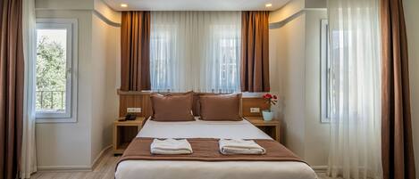 Habitación de hotel con una cama grande, mesitas de noche, una ventana con cortinas y vistas a zonas verdes.