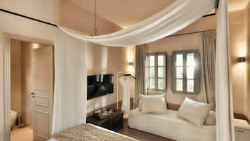 A bedroom with a canopy bed, a sofa, a TV, and a bedside table with glasses.