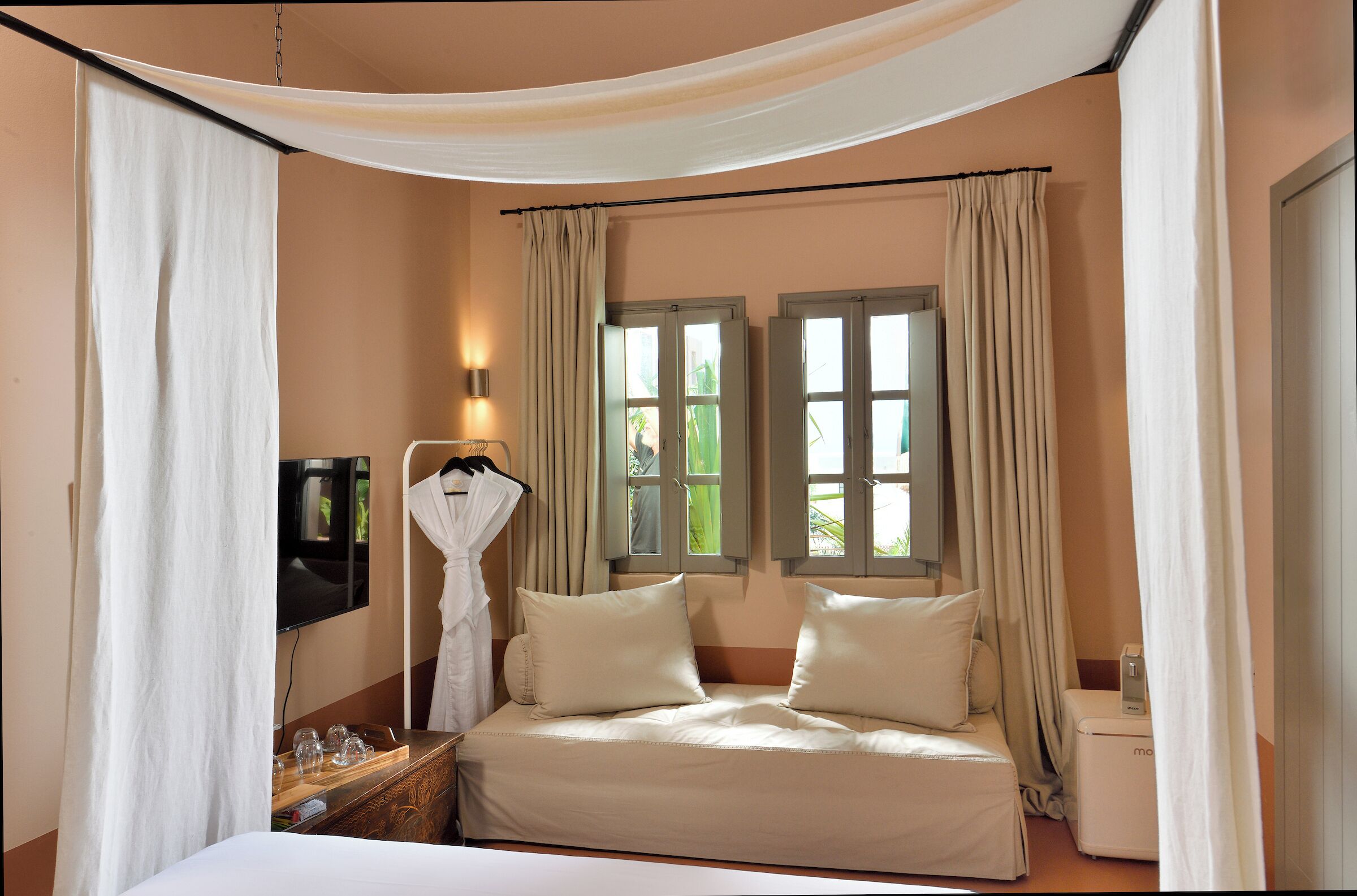 A bedroom with a bed, a bedside table with glasses, a TV, and a window with curtains.