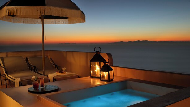 A balcony with a hot tub, lounge chairs, and a table with drinks and fruit. - Terra Verde Oia by K&K (Santorini)
