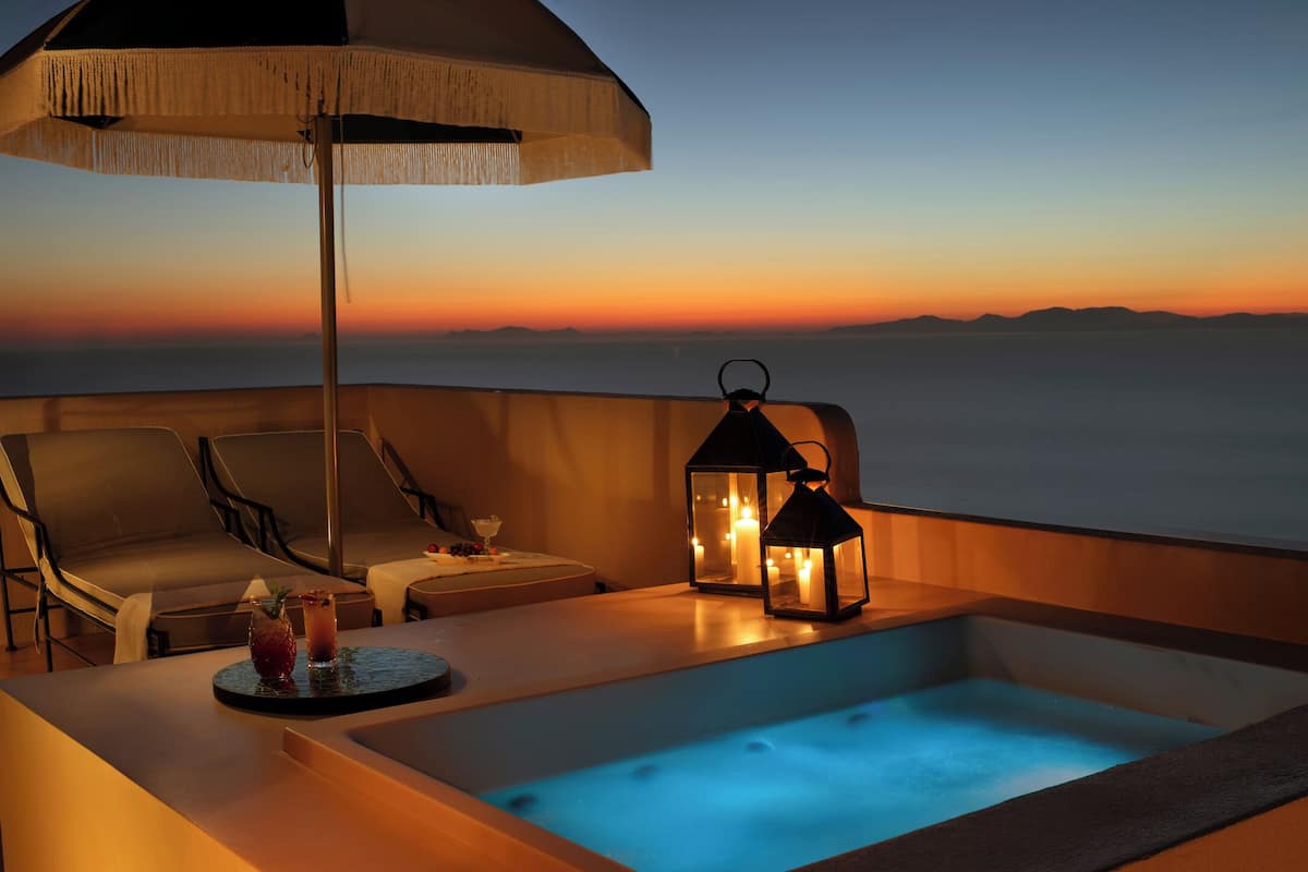 Een balkon met een jacuzzi, lounge stoelen en een tafel met drankjes en fruit.