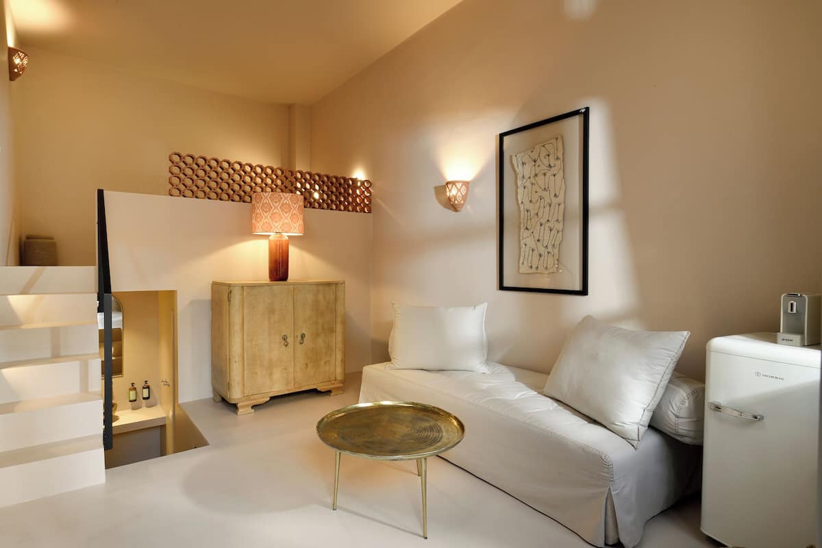 Een moderne woonkamer met een witte bank, een ronde salontafel, een houten kast en een kleine koelkast.