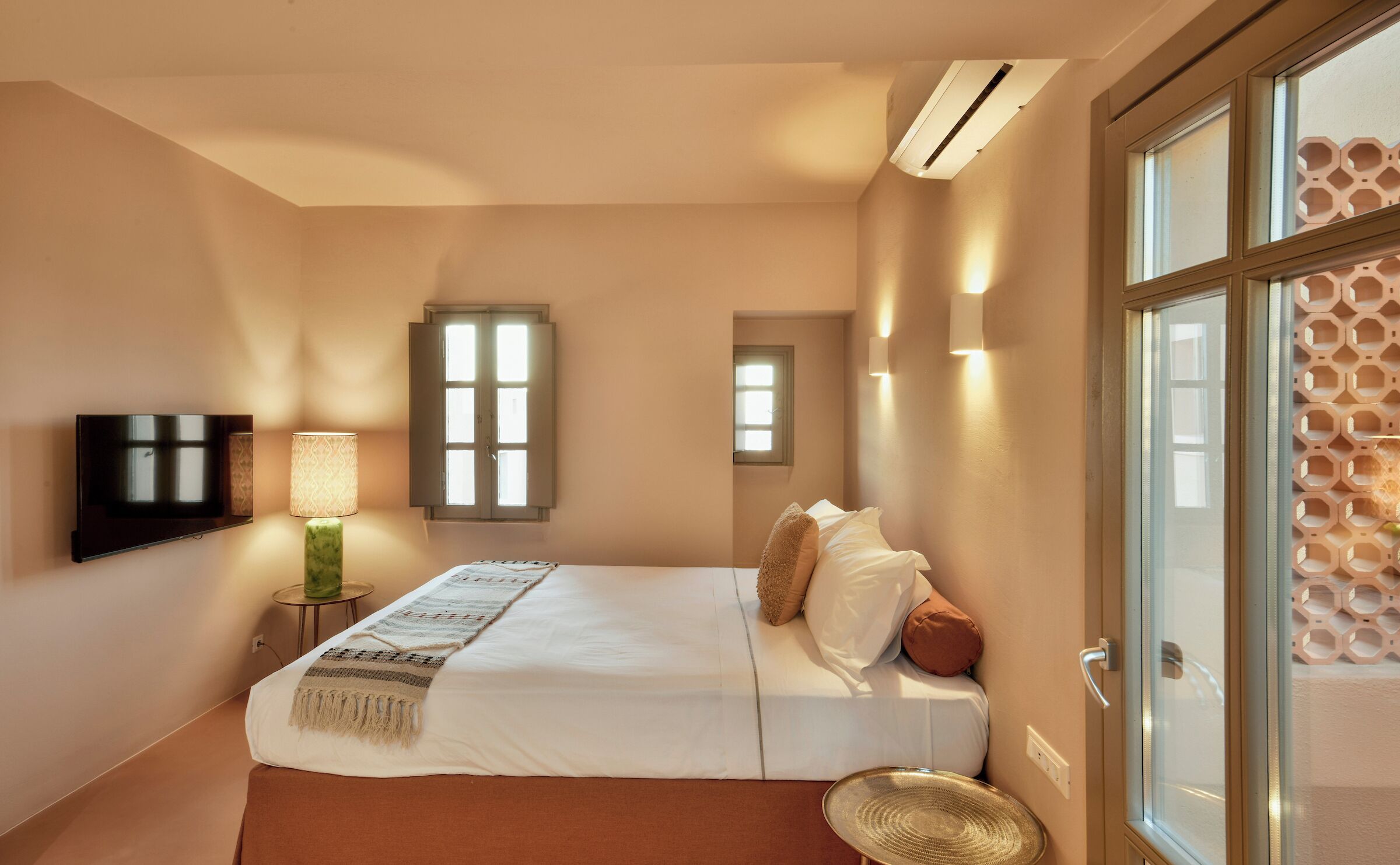 A bedroom with a bed, a TV, a lamp, and a window.