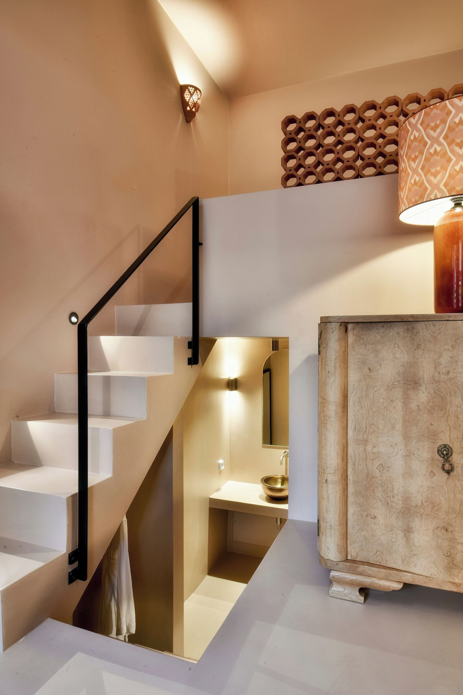 A staircase with a black metal railing leading to a landing. A wooden cabinet with a brass handle is visible on the landing.