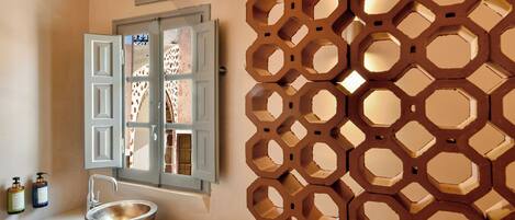 A bathroom with a sink, a window with open shutters, and a decorative wall panel.