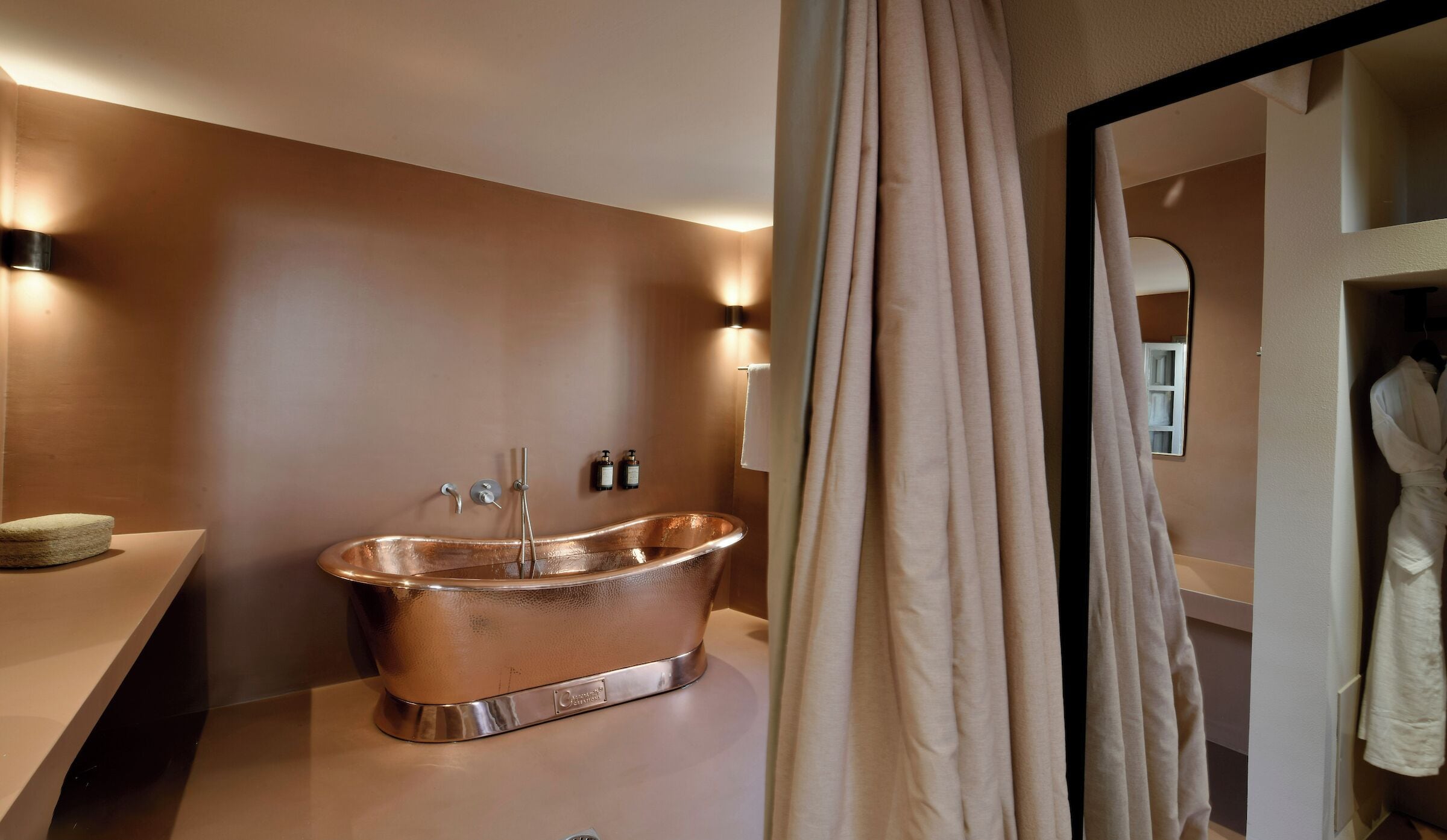 Une salle de bain moderne avec une baignoire en cuivre, un meuble-lavabo avec un miroir et un peignoir suspendu à un porte-peignoir.