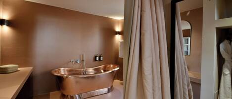 Une salle de bain moderne avec une baignoire en cuivre, un meuble-lavabo avec un miroir et un peignoir suspendu à un porte-peignoir.