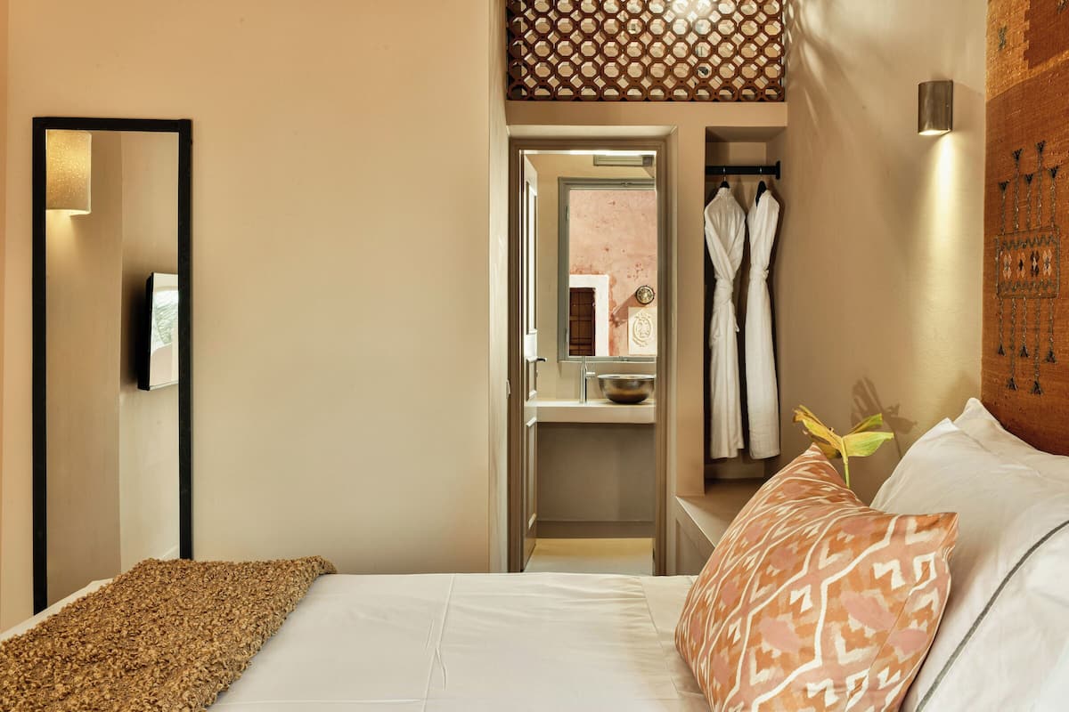 Hotelkamer met een bed, een spiegel, een kledingkast en een kleine badkamer die door een open deur zichtbaar is.