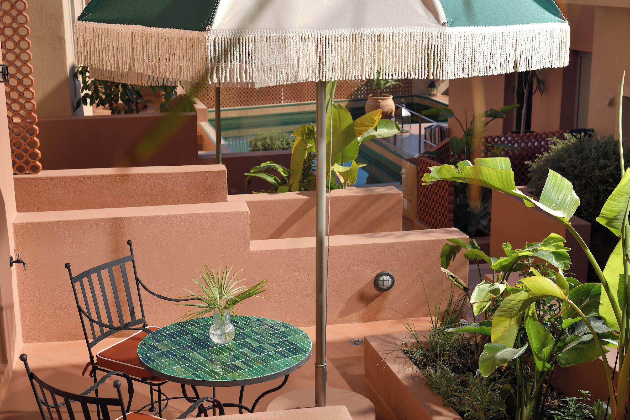 A patio with a round table, chairs, a hanging umbrella, and potted plants.