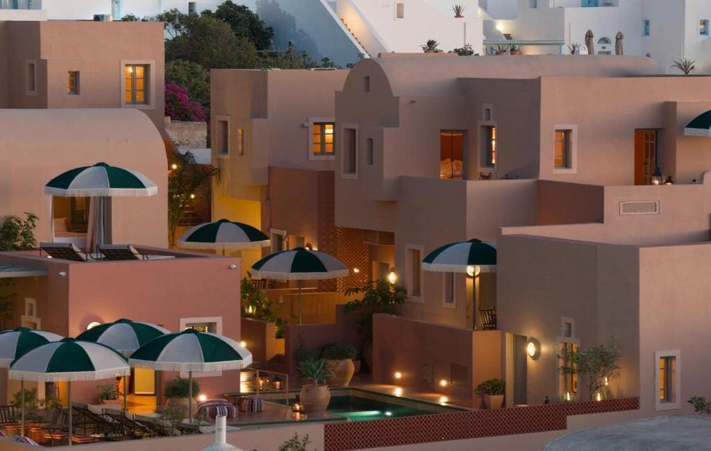 Un resort con varias edificaciones, zonas de estar al aire libre con sombrillas y una piscina.