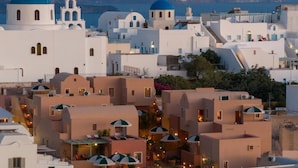 A coastal town with white buildings and blue domes, featuring a central courtyard with umbrellas and a pool. - Terra Verde Oia by K&K (Santorini)