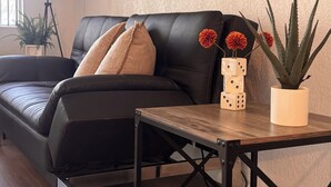 A living room with a black leather sofa, a wooden coffee table, and three framed pictures on the wall.