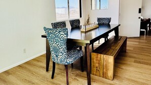 A spacious dining area with a wooden table and patterned chairs, large windows, and a ceiling light fixture.